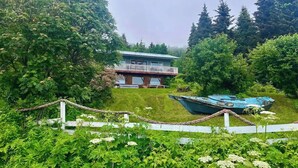 Une maison dotée d’un balcon, entourée d’une végétation luxuriante, avec un bateau en premier plan.