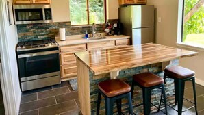 Une cuisine moderne avec des meubles en bois, un réfrigérateur en acier inoxydable, un four encastré et un grand îlot central doté de tabourets.
