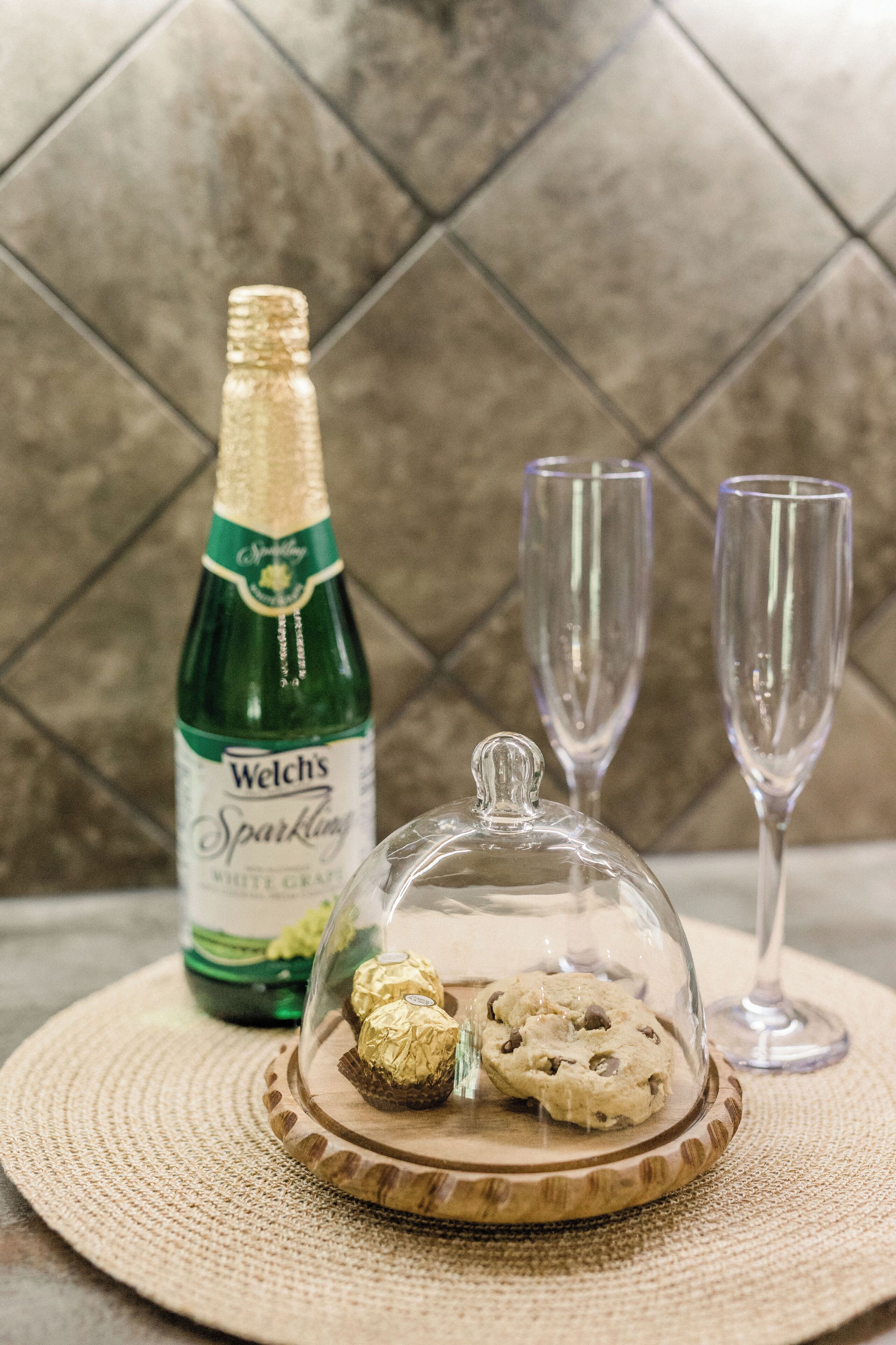 A bottle of Welch's Sparkling wine, two glasses, and a wooden tray with cookies and a glass dome.