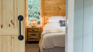 A wooden room with a bed, a nightstand, a window, and a door.