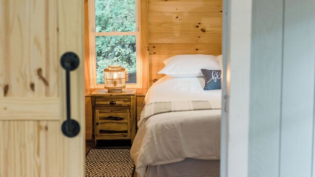 Une pièce en bois avec un lit, une table de chevet, une fenêtre et une porte.