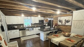 Une cuisine spacieuse avec des poutres en bois, des armoires blanches et un coin repas avec une table dressée pour quatre personnes.