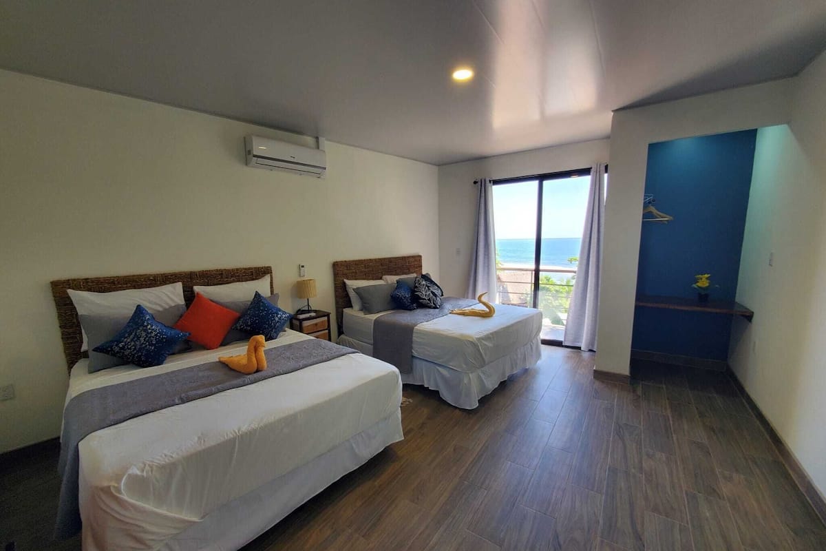 A hotel room with two beds, a balcony with a view, and a blue door.