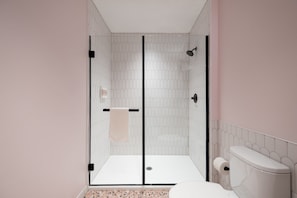 Bathroom features a glass-enclosed shower, white toilet, and speckled tile floor.