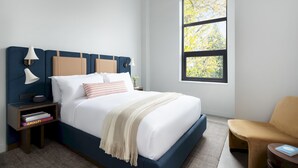 Een netjes ingerichte slaapkamer met een groot bed, bedlampen, een stoel en een raam met uitzicht op bomen.