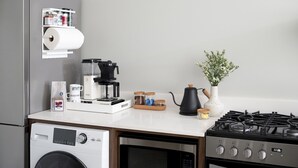 Een keuken met een koelkast, koffiezetapparaat, waterkoker en een gasfornuis.