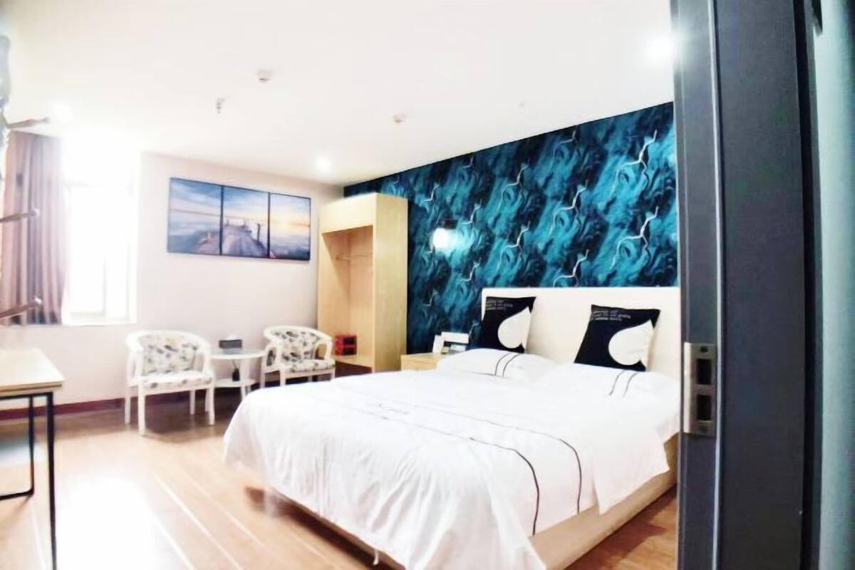 A hotel room with a bed, a desk, two chairs, a small table, and a wall with a blue abstract design.
