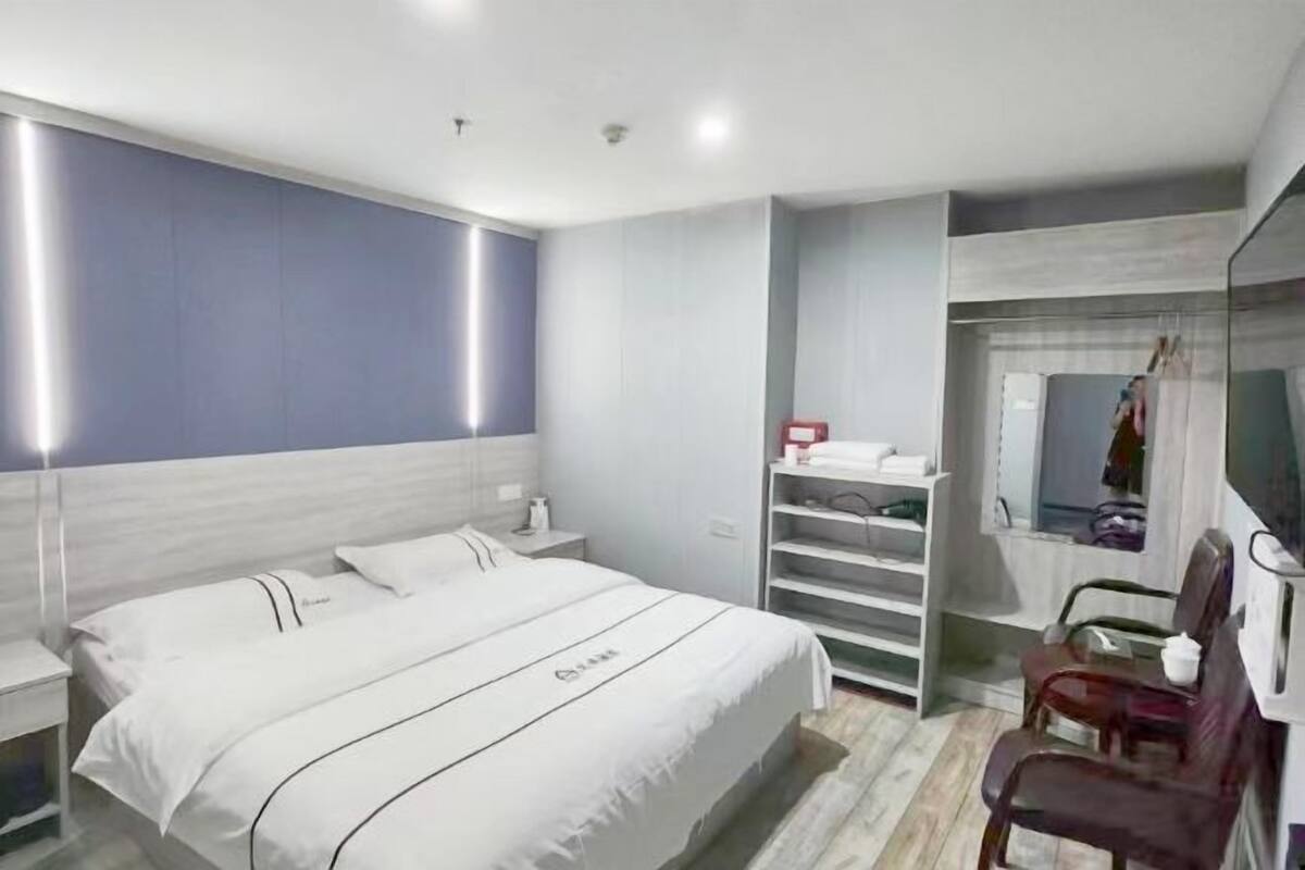A modern hotel room with a bed, bedside tables, a wardrobe, and a mirror.