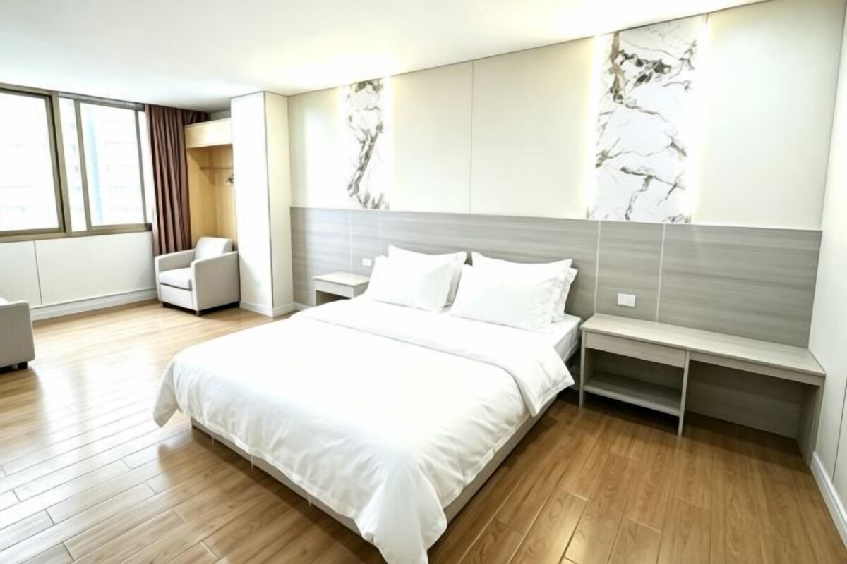 A modern bedroom with a large bed, bedside tables, a seating area, and a view of the outdoors.