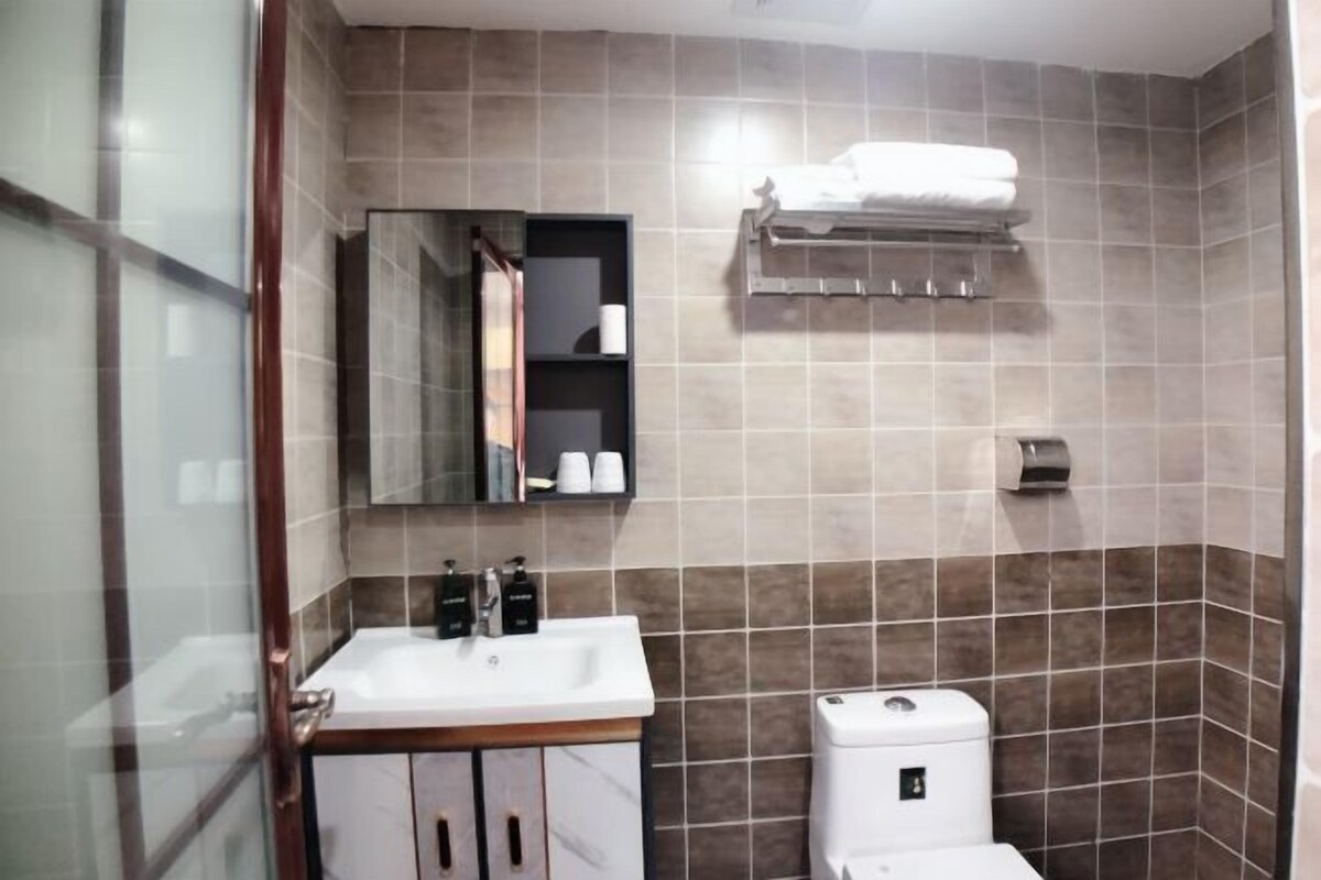 Um banheiro moderno com box de vidro, pia branca com bancada de mármore, espelho acima da pia e porta-toalhas na parede.