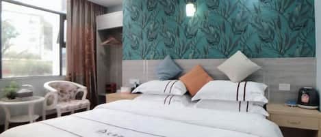 A hotel room with a bed, bedside table, chair, and a view of the outdoors.