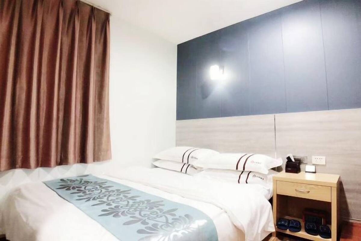 A hotel room with a bed, a nightstand, and a wall-mounted light.