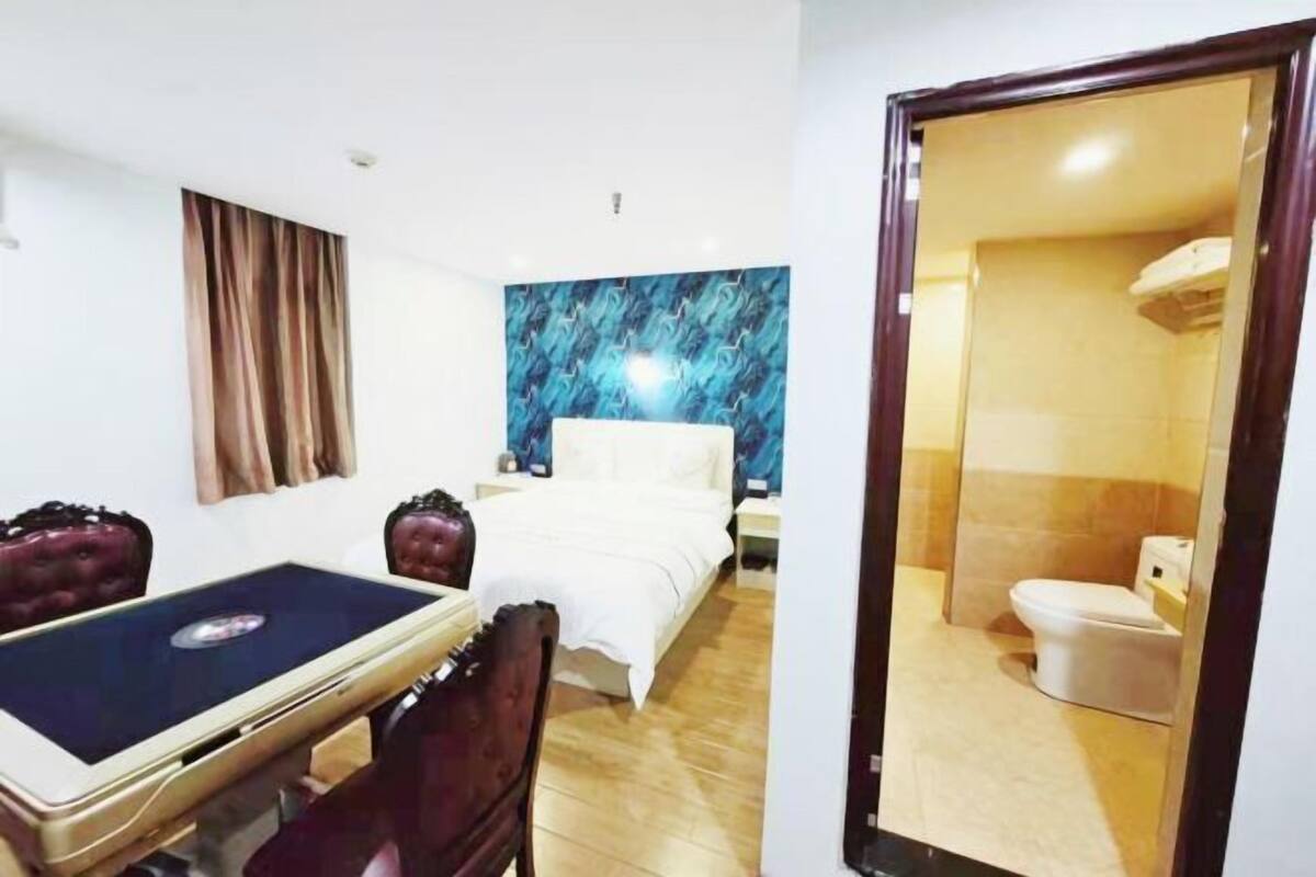 A hotel room with a bed, a bedside table, a mirror, and a bathroom visible through an open door.