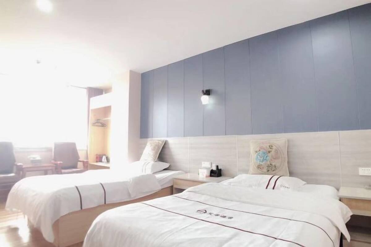 A hotel room with two beds, a bedside table, a nightstand, a wall-mounted light, and a window with a view.