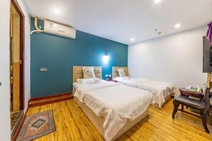 A hotel room with two beds, a wooden floor, a wall-mounted air conditioner, and a small table with a chair. - AiXi Traving with hostel (Chongqing)