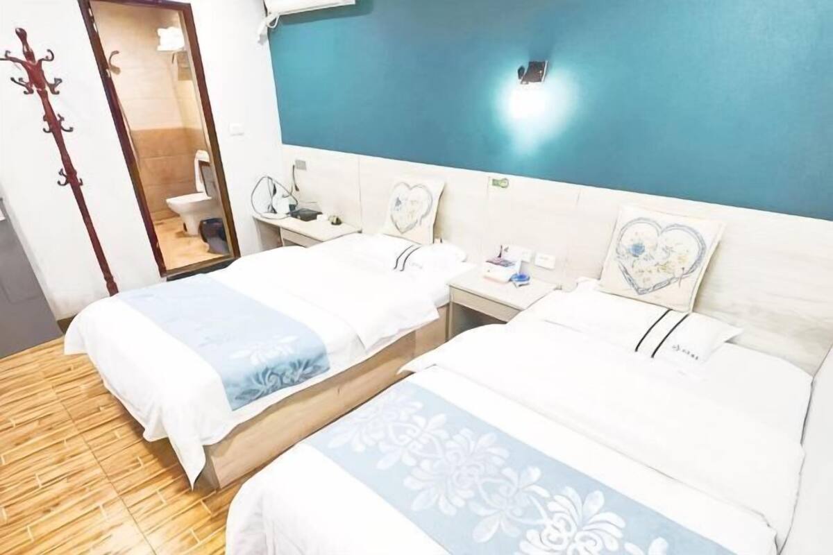 A hotel room with two beds, a bathroom, a mirror, and a blue wall.