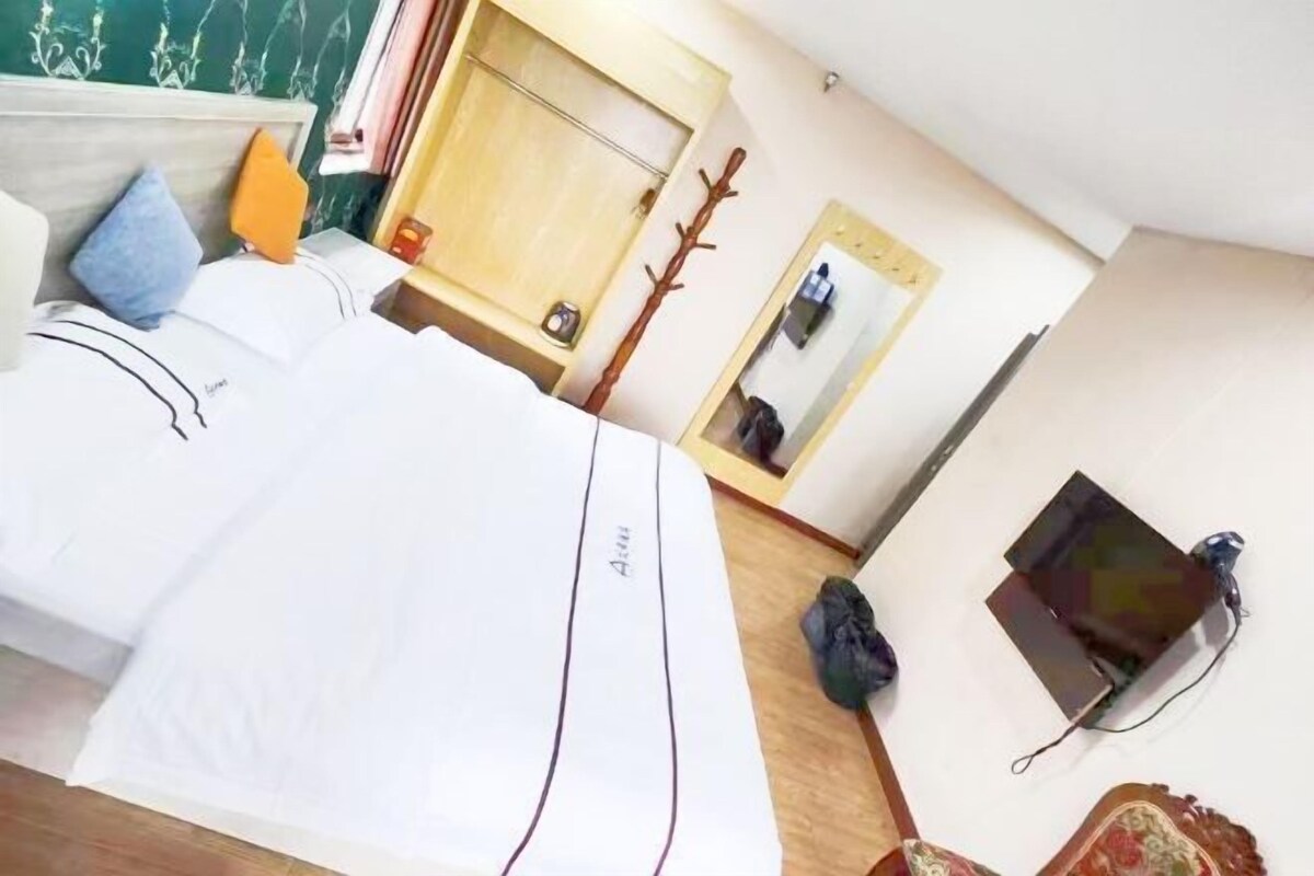 A hotel room with a bed, a wooden headboard, a mirror, a coat rack, and a small table with a cup.