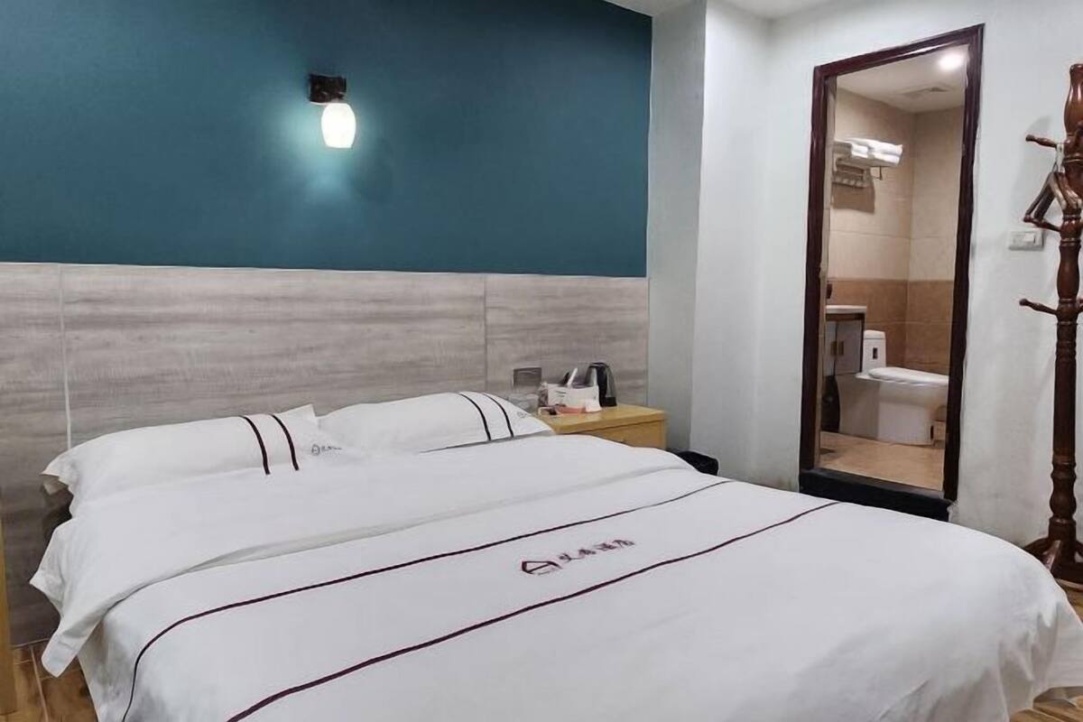 A hotel room with a bed, a nightstand, a mirror, and a view of the bathroom.
