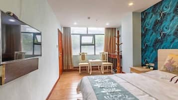 Habitación de hotel con cama, escritorio con sillas, televisor montado en la pared y un ventanal grande.