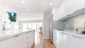 Une cuisine moderne avec des meubles blancs, un plancher en bois et un vase de fleurs bleues posé sur le comptoir.