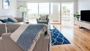 Un salon moderne avec un canapé, un fauteuil et un téléviseur, un balcon avec vue et un tapis bleu à motifs.