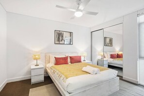 A hotel room with a bed, bedside lamps, a ceiling fan, a large mirror, and artwork on the wall.