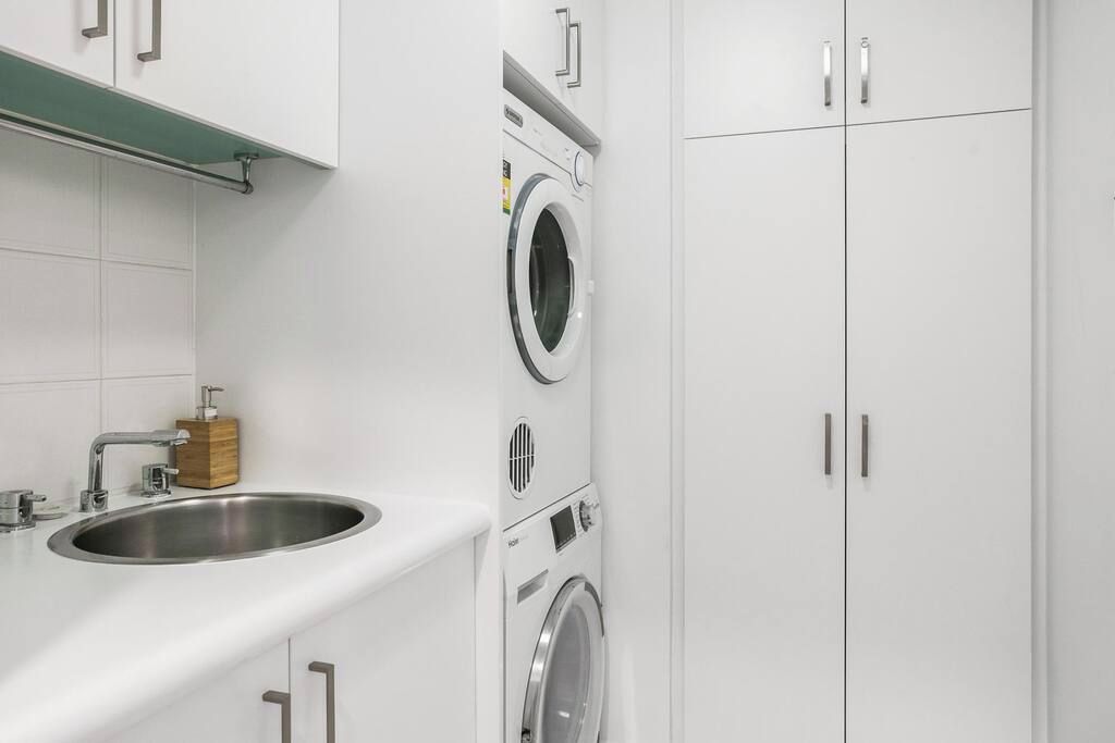 A modern laundry room with a stainless steel sink, a washing machine, and a dryer.