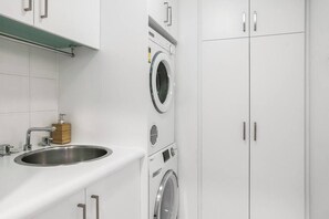 Een moderne wasruimte met een roestvrijstalen spoelbak, een wasmachine en een droger.
