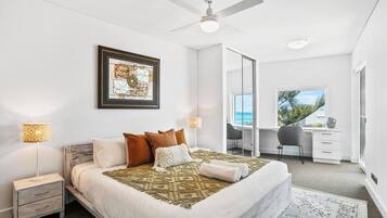 Une chambre à coucher comprenant un lit, des tables de chevet, un ventilateur de plafond, une œuvre d’art encadrée et une vue sur l’extérieur.