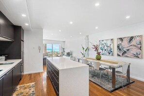 A modern kitchen with a central island, a dining area with a table and chairs, and artwork on the walls. - Apartment M401 - coastal style and luxury awaits! (Scarborough)