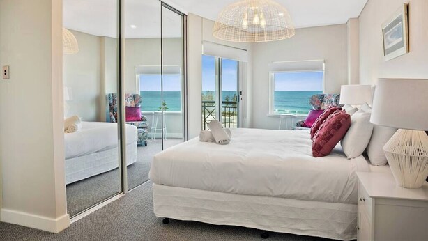 A modern bedroom with a large bed, a glass door leading to a balcony, and a view of the ocean. - Apartment M503 - panoramic ocean views for miles! (Scarborough)