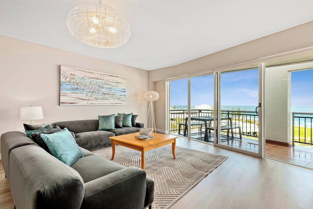 A modern living room with a sofa, coffee table, and a large window offering a view of the ocean.