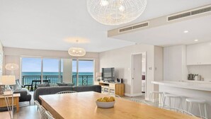 A modern living room with a wooden dining table, a sofa, and a TV. There is a balcony with a view of the sea. - Apartment M503 - panoramic ocean views for miles! (Scarborough)