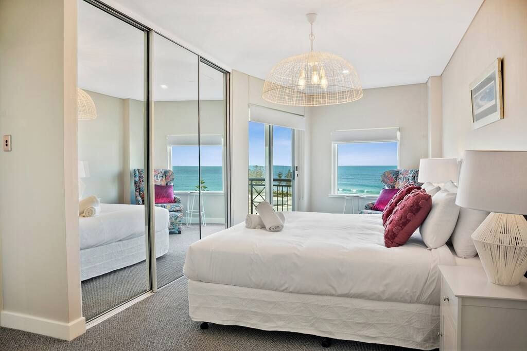 Un dormitorio con una cama grande, un ventanal de vidrio que da a un balcón y vistas al mar.