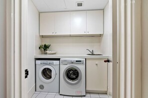 A compact laundry room with two front-loading washing machines, a sink, and a small countertop with a plant. - Apartment M503 - panoramic ocean views for miles! (Scarborough)