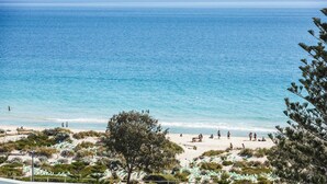Una playa con agua azul cristalina, orilla de arena y algo de vegetación.