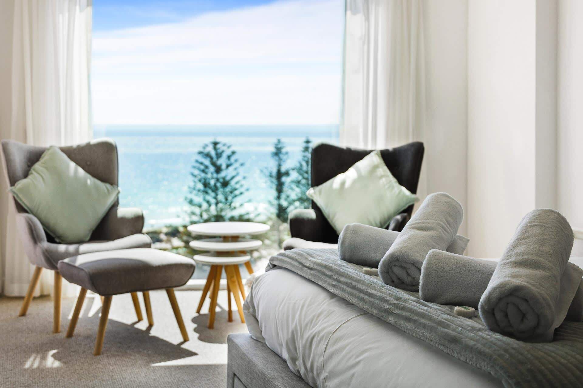 A modern living room with a sofa, two armchairs, a small round table, and a view of the ocean.