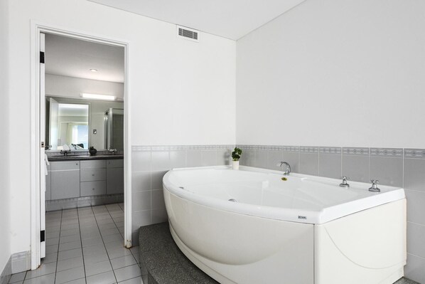 A modern bathroom with a large white bathtub, grey tiled walls, and a visible doorway leading to another room.