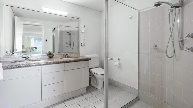 Ein modernes Badezimmer mit Duschkabine aus Glas, einem großen Spiegel und einer Arbeitsplatte aus Granit.