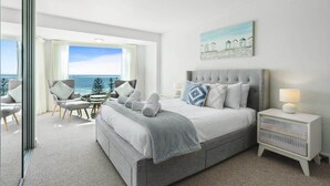 Un dormitorio con una cama grande, una mesita de noche, una silla y vistas al mar.