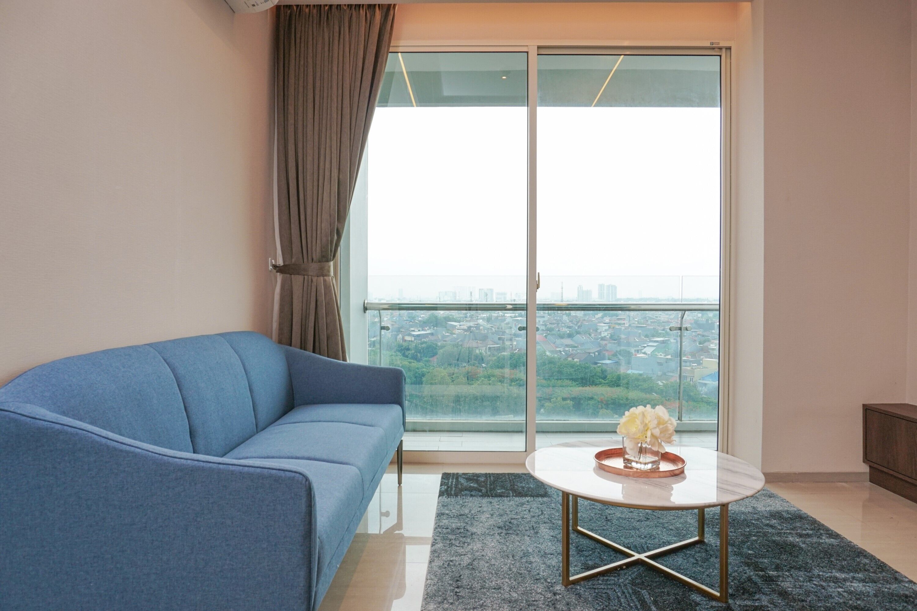 Un salon moderne avec un canapé bleu, une table basse ronde blanche et une vue sur le paysage urbain, visible à travers une grande porte vitrée.