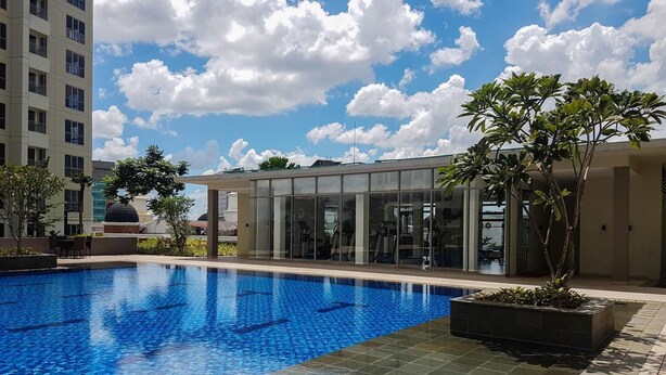 Ein Schwimmbecken mit klarem, blauem Wasser, umgeben von einem modernen Gebäude mit Glasfenstern und einer gefliesten Terrasse.