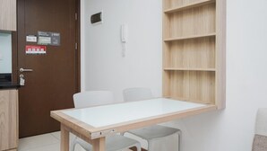 Ein kleiner, sauberer Raum mit einem Holztisch, zwei Stühlen, einem Holzregal, einer Tür mit Schloss und einem Telefon an der Wand.