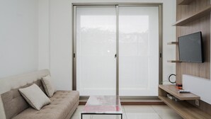 Ein modernes Wohnzimmer mit einer Schiebetür aus Glas, einem beigen Sofa, einem kleinen Couchtisch und einem an einer Holzablage montierten Fernseher.