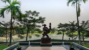 A statue in a park with a pond and palm trees. - Minimalist And Comfy 1Br Citralake Suites Apartment (Jakarta)