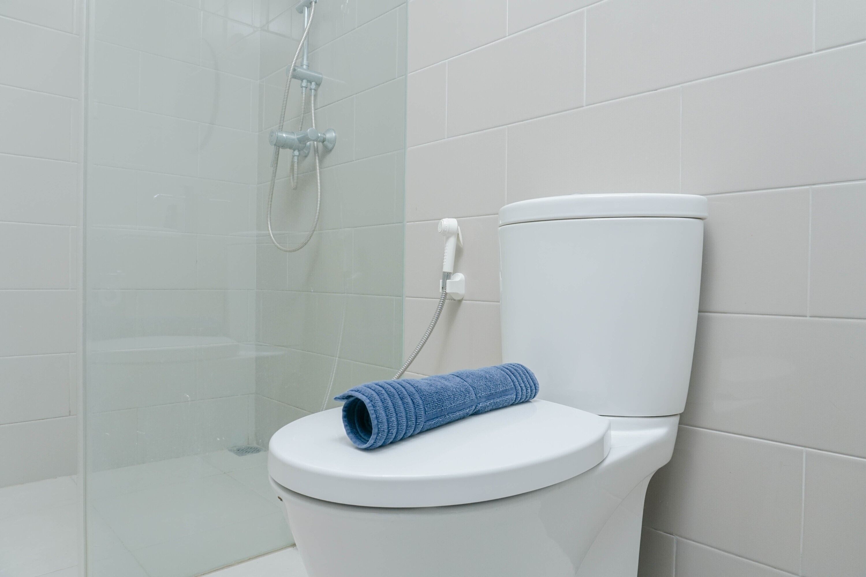 A modern bathroom with a white toilet, a glass shower enclosure, and a blue towel on the toilet seat.