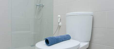 A modern bathroom with a white toilet, a glass shower enclosure, and a blue towel on the toilet seat.