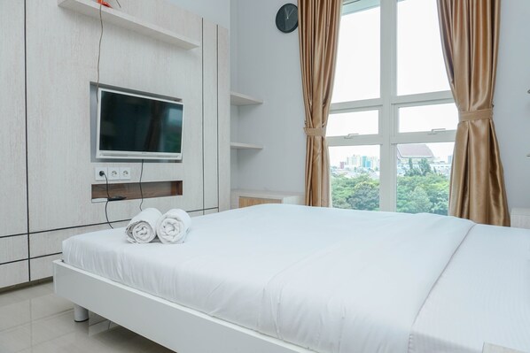 A modern hotel room with a large bed, a flat-screen TV mounted on the wall, and a window with curtains.