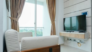 A modern living room with a sofa, a TV mounted on a wooden panel, and a large window with curtains. - Minimalist And Comfy 1Br Citralake Suites Apartment (Jakarta)