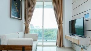 A modern living room with a sofa, a TV on a wooden stand, and a large window with curtains. - Minimalist And Comfy 1Br Citralake Suites Apartment (Jakarta)
